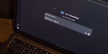 A laptop on a wooden table shows an AI chat interface, featuring the DeepSeek chatbot in action.