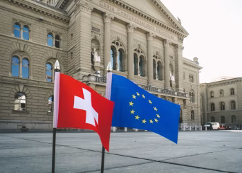 Front view of Swiss Parliament Building in Bern with Swiss and EU flags.