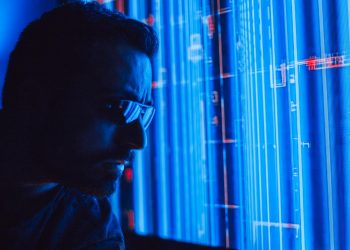 A man in sunglasses intently studies a vibrant blue holographic screen, symbolizing digital technology.
