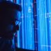 A man in sunglasses intently studies a vibrant blue holographic screen, symbolizing digital technology.