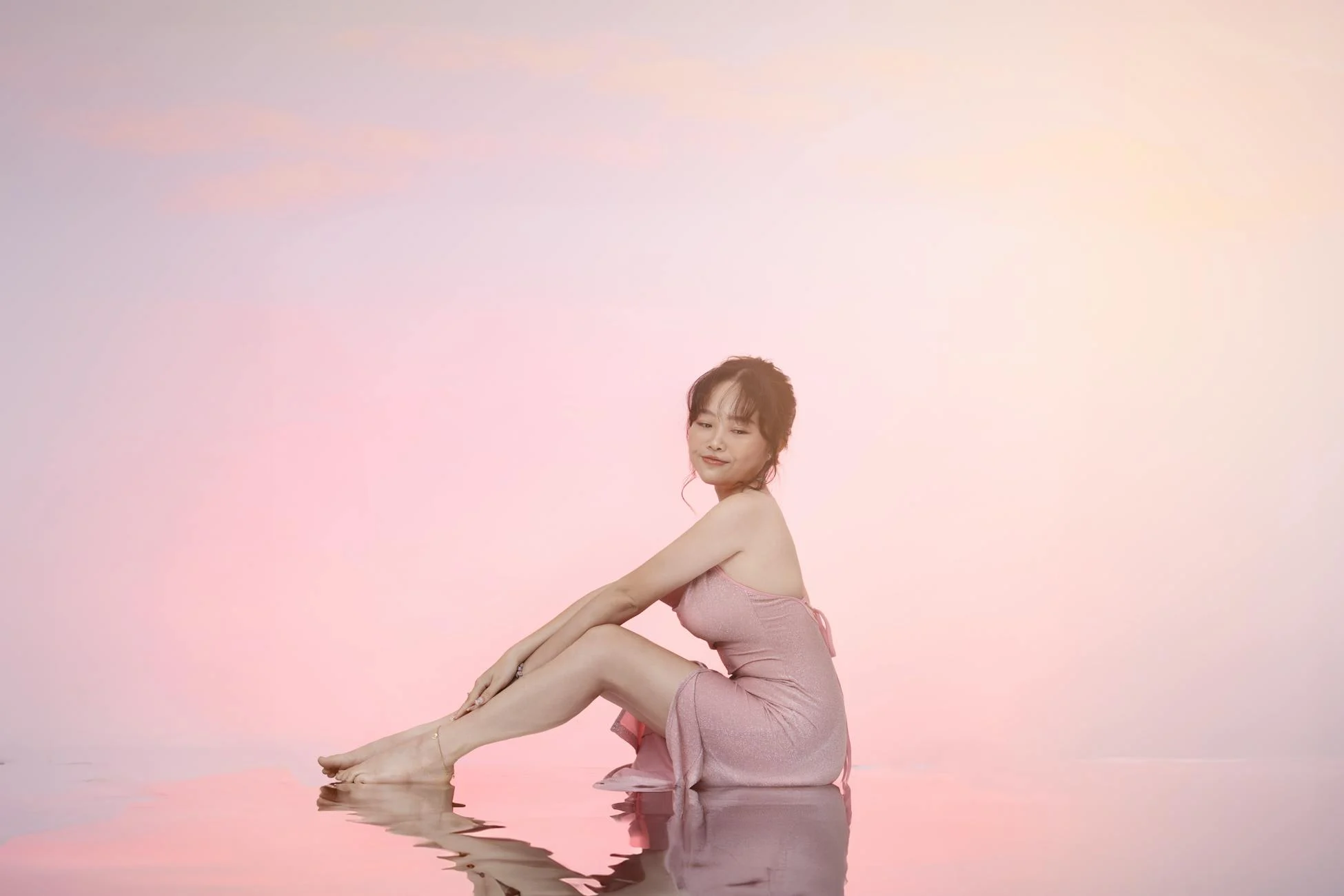 A woman gracefully poses in a pink dress against a pastel background, reflecting beauty and serenity.