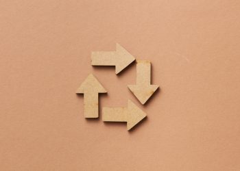 Close-up of a recycling symbol made from wooden arrows on a beige background.