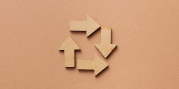 Close-up of a recycling symbol made from wooden arrows on a beige background.
