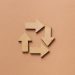Close-up of a recycling symbol made from wooden arrows on a beige background.