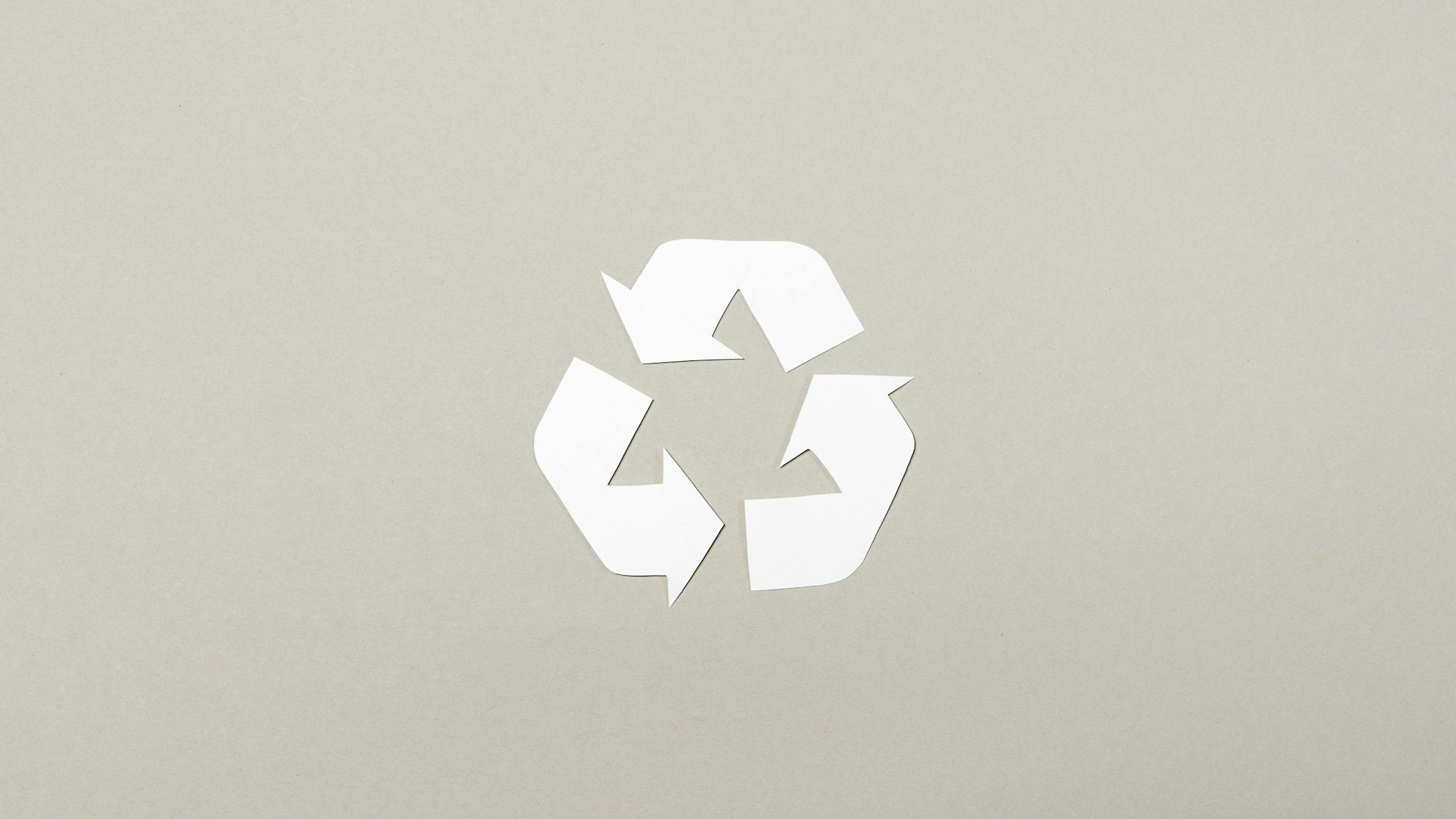 Simple paper cutout recycle symbol on a neutral gray background, emphasizing sustainability.