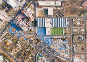 A stunning overhead shot of a sports complex with tennis courts, football field, and nearby park facilities.