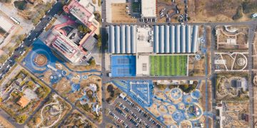 A stunning overhead shot of a sports complex with tennis courts, football field, and nearby park facilities.