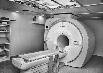 Black and white image of a modern MRI machine in a hospital room with overhead ceiling art.