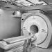 Black and white image of a modern MRI machine in a hospital room with overhead ceiling art.