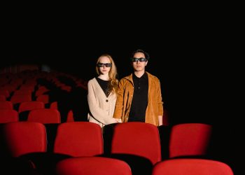 Interracial couple with 3D glasses watching a movie in an empty cinema.