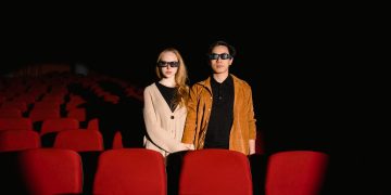 Interracial couple with 3D glasses watching a movie in an empty cinema.