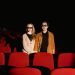 Interracial couple with 3D glasses watching a movie in an empty cinema.