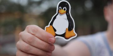 A close-up shot of a hand holding a penguin sticker against a blurred outdoor background.