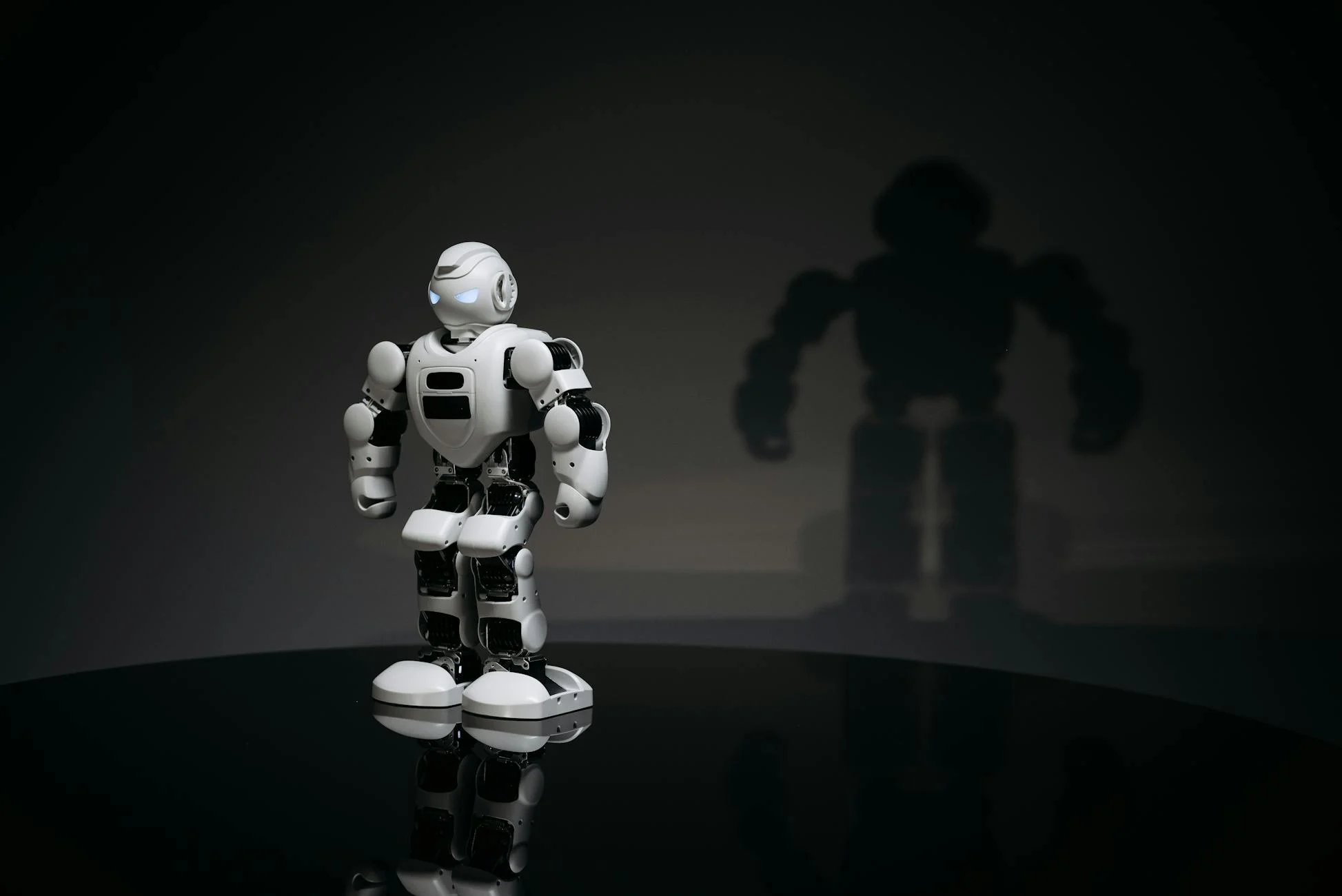 A white and black toy humanoid robot in a studio setting casting a shadow.