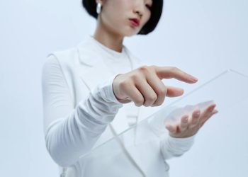 Woman touches transparent interface in a modern, futuristic setting.