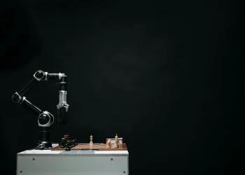 An articulated robotic arm competes in chess on a board against a dark background, highlighting AI and innovation.