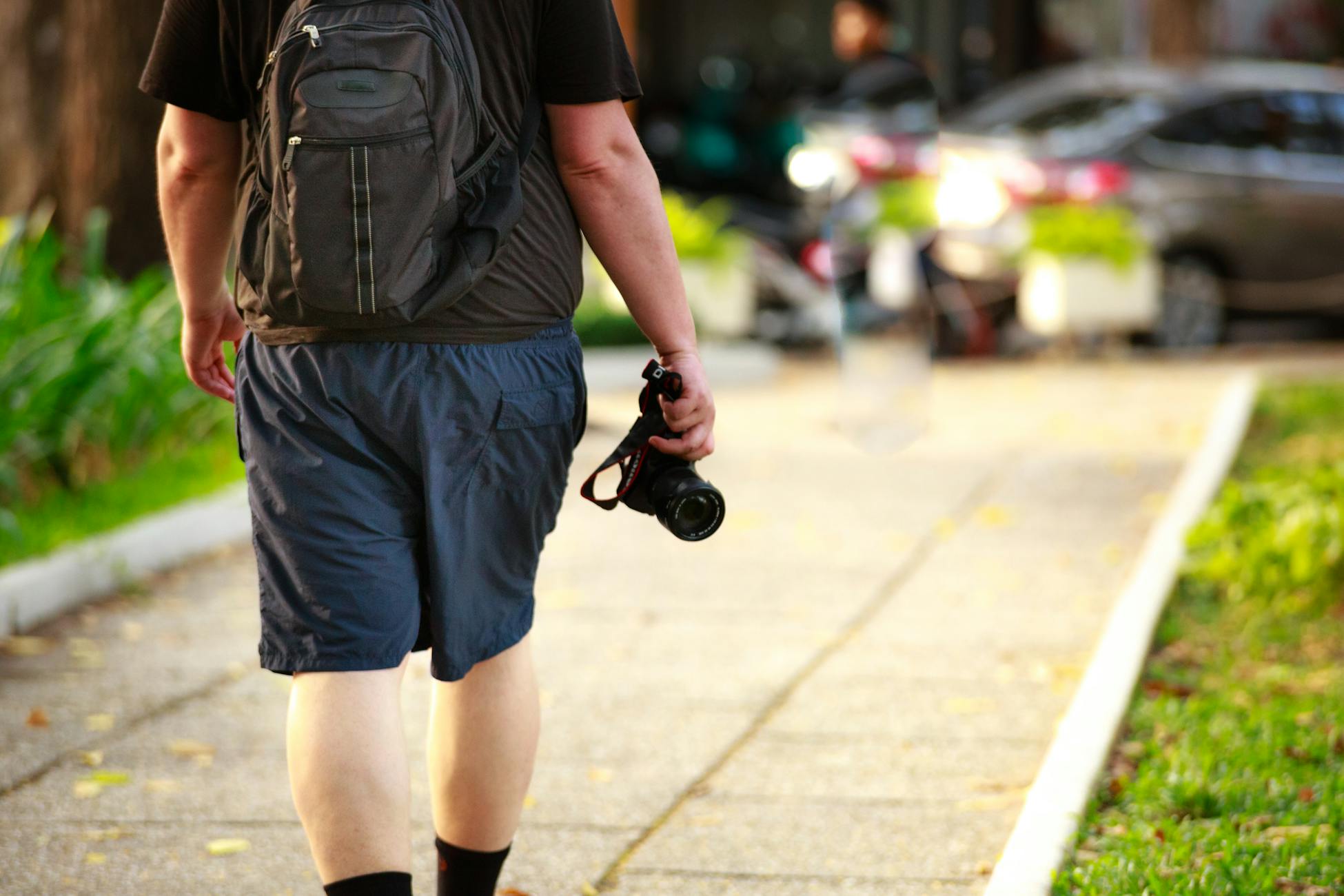 Man walking outdoors with a camera and backpack on a sunny day.