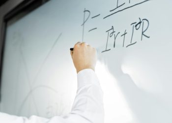 Close-up of a hand writing a formula on a whiteboard in a professional setting.