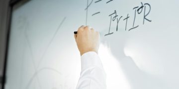 Close-up of a hand writing a formula on a whiteboard in a professional setting.