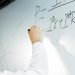 Close-up of a hand writing a formula on a whiteboard in a professional setting.