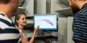 Three engineers discussing sound waves displayed on a monitor in a professional sound studio.