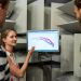 Three engineers discussing sound waves displayed on a monitor in a professional sound studio.