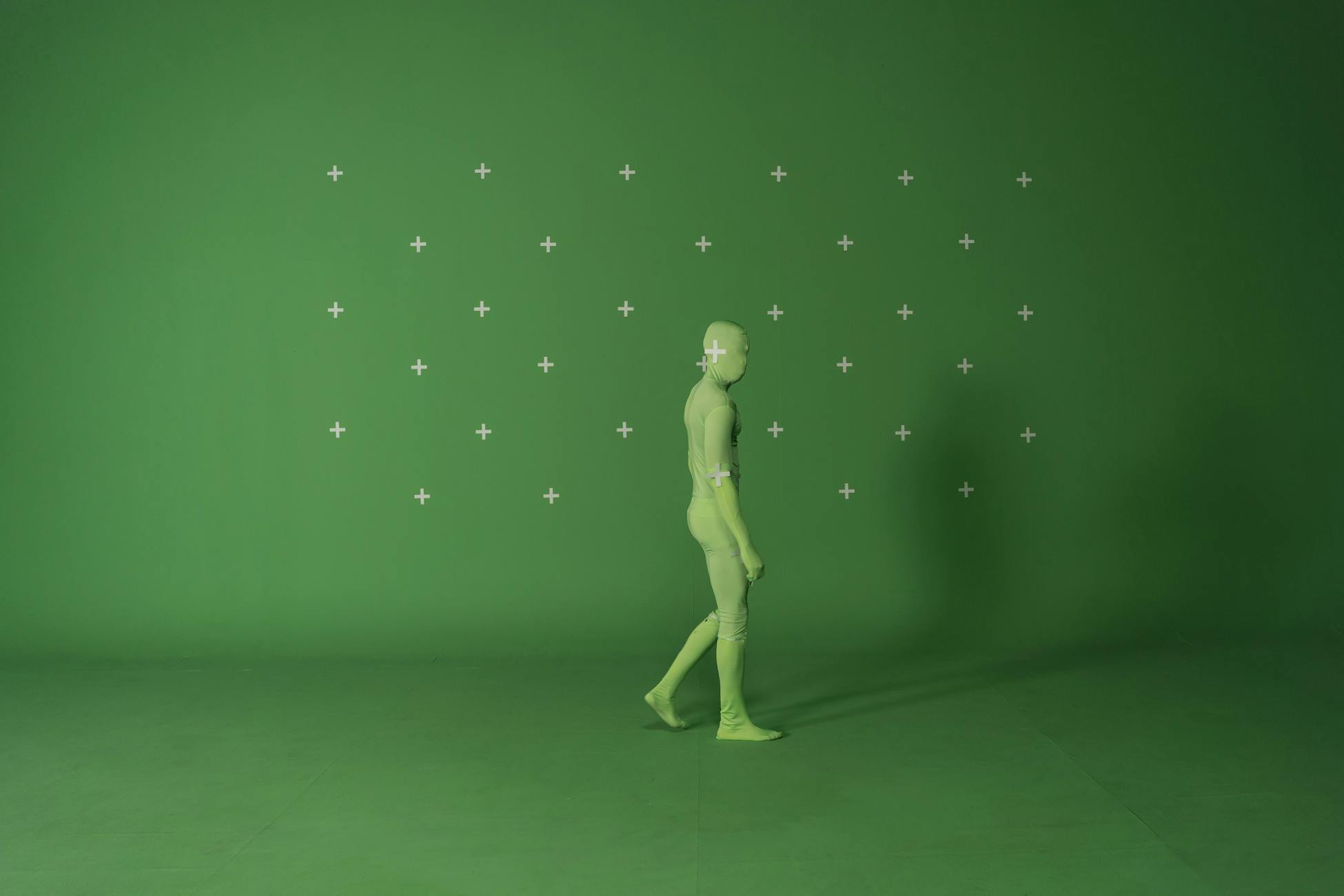 Person walking in a chroma key suit in a studio with green screen for video editing.