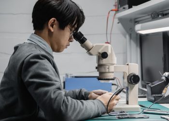 A focused technician repairing electronic components with a microscope in a lab.