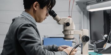A focused technician repairing electronic components with a microscope in a lab.