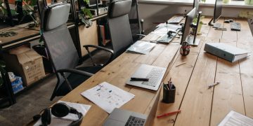 Spacious co-working office with wooden desks, laptops, and modern chairs.