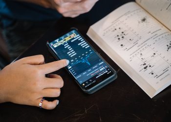 Hand pointing at smartphone displaying financial data, with open book nearby.