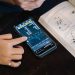 Hand pointing at smartphone displaying financial data, with open book nearby.