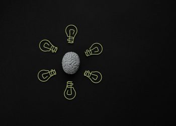 Conceptual photo of a brain surrounded by light bulb clips on black background.