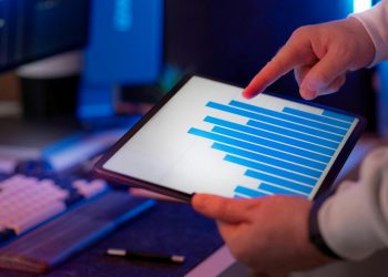 Business professional analyzing bar chart on tablet in office setting, highlighting data insights.
