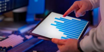 Business professional analyzing bar chart on tablet in office setting, highlighting data insights.