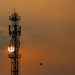 Silhouette of a telecommunication tower against a vibrant sunset sky with a distant kite.