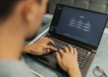 A focused individual types on a laptop running AI software indoors.