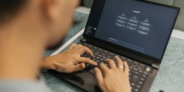 A focused individual types on a laptop running AI software indoors.