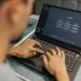 A focused individual types on a laptop running AI software indoors.