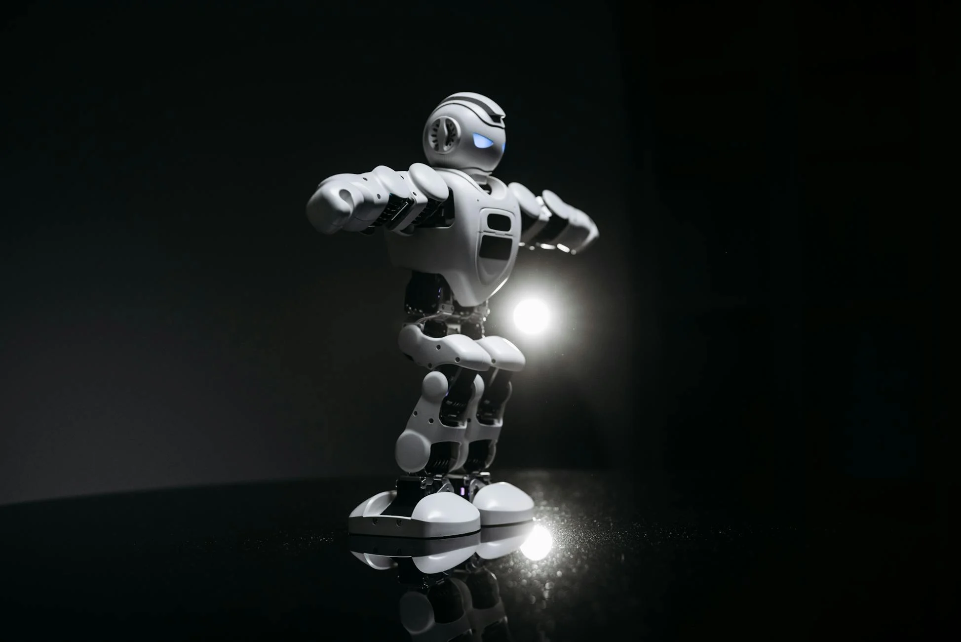White humanoid robot with glowing eyes standing on a reflective black surface in studio lighting.
