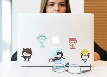 GitHub 스티커가 붙은 노트북 앞 안경 — GitHub Copilot 토큰 종량제