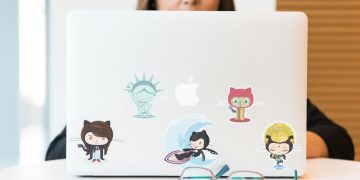 GitHub 스티커가 붙은 노트북 앞 안경 — GitHub Copilot 토큰 종량제