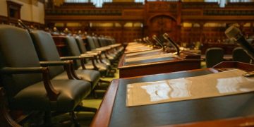 A detailed view of an empty legislative chamber with rows of desks and microphones, evoking governance.