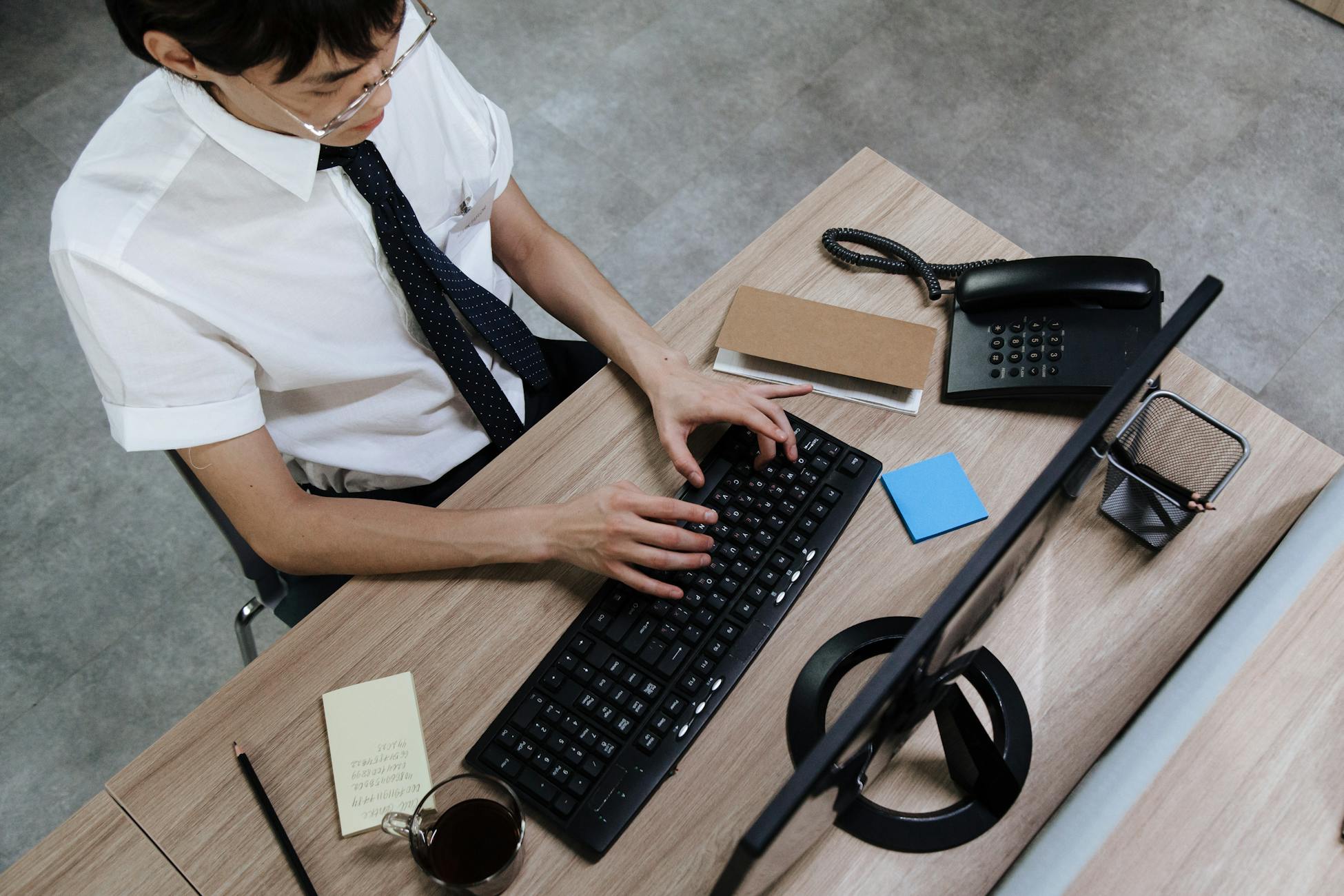 Asian man in business attire typing on a keyboard at a modern office desk.