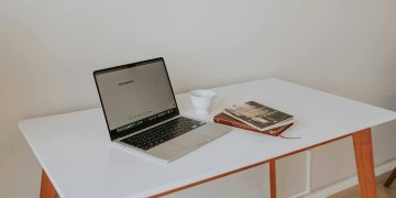 A minimalistic workspace featuring a laptop, coffee cup, and books on a white de