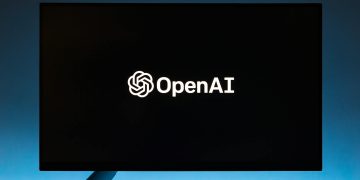 Minimalist display of OpenAI logo on a screen, set against a gradient blue background.