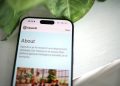 Close-up shot of a smartphone screen showing the OpenAI website with greenery in the background.