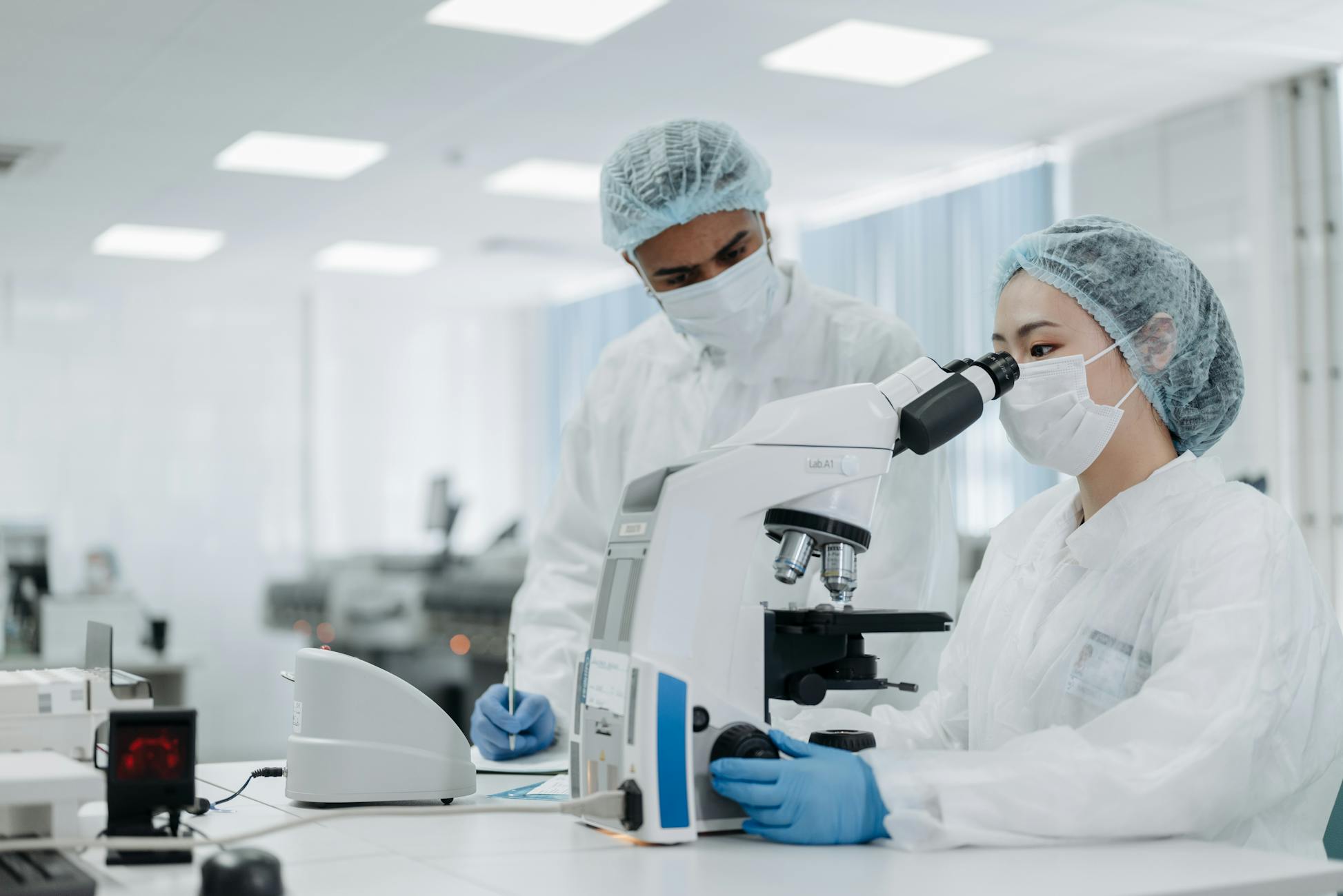 Scientists in protective suits examining samples under a microscope, focusing on microbiological research.