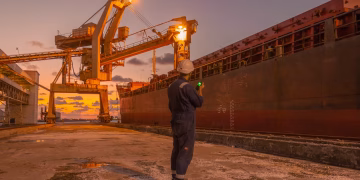 A dock worker examines a cargo ship under twilight skies at a Libyan port, highlighting industrial operations.