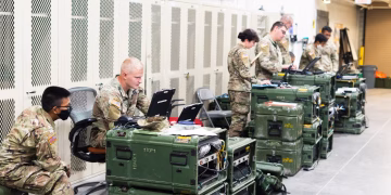 A group of military personnel in uniforms using computers and communication equipment in a secure indoor facility.